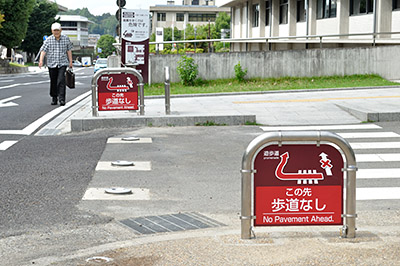 防止柵や誘導看板が設置された奈良市道。撤去された歩道は男性が歩いている所にあった。右は奈良県庁