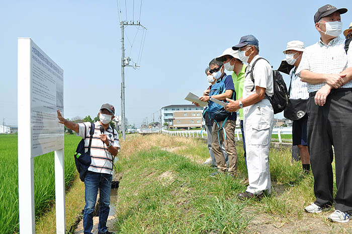 柳本飛行場跡を歩く催しで説明に耳を傾ける参加者。左が市民団体が設置した説明板＝2020年8月6日、奈良県天理市長柄町