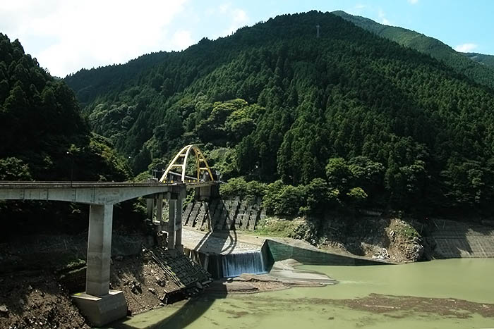 大滝ダム湖（手前）、そして橋の向こうに高原トンネルの入り口（中央奥）。橋の下には迫地区の地滑り対策のアンカー工が見える＝2020年9月8日、奈良県川上村