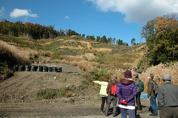 森林が伐採され、土のうが置かれたメガソーラー建設現場を見学する人たち＝2021年11月23日、平群町