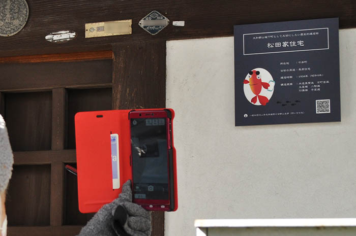 町家に掲示された表示板のQRコードにスマートフォンを向ける町歩きの参加者＝2022年3月6日、奈良県大和郡山市（画像の一部を修正しています）