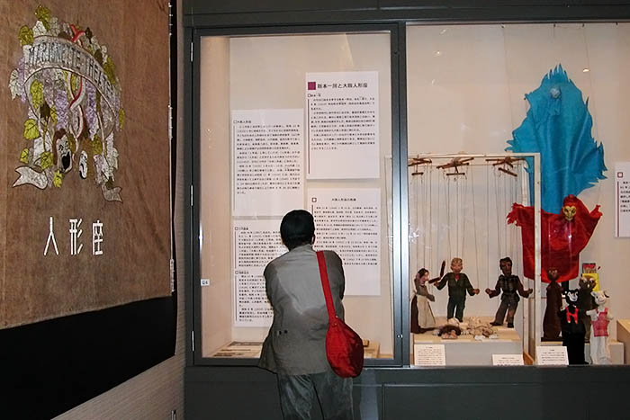 赤い衣装をまとった人形（火の精）は阪本一房の作。壁面の緞帳は戦前の大阪人形座が使用していた＝2022年4月29日、吹田市岸部北4丁目の同市立博物館