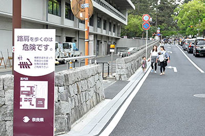 歩道が撤去された奈良市道に奈良県が設置した迂回路の案内看板と車道を歩く人