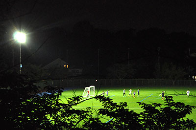 夜間照明がついた生駒北スポーツセンターグラウンド。照明によって周辺の住宅建物が浮かび上がる。選手の掛け声も住宅地にこだましていた