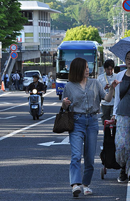 路肩の白線を車道側に越えて歩く通行者とその後方から迫る観光バス＝2019年5月4日、奈良市登大路町