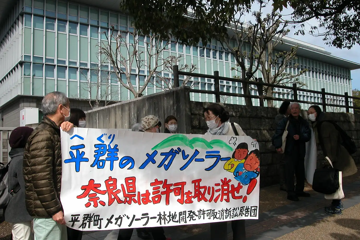 奈良地裁前で県のメガソーラー許可取り消しを求めて横断幕を掲げる住民ら＝2024年3月7日、奈良市登大路町