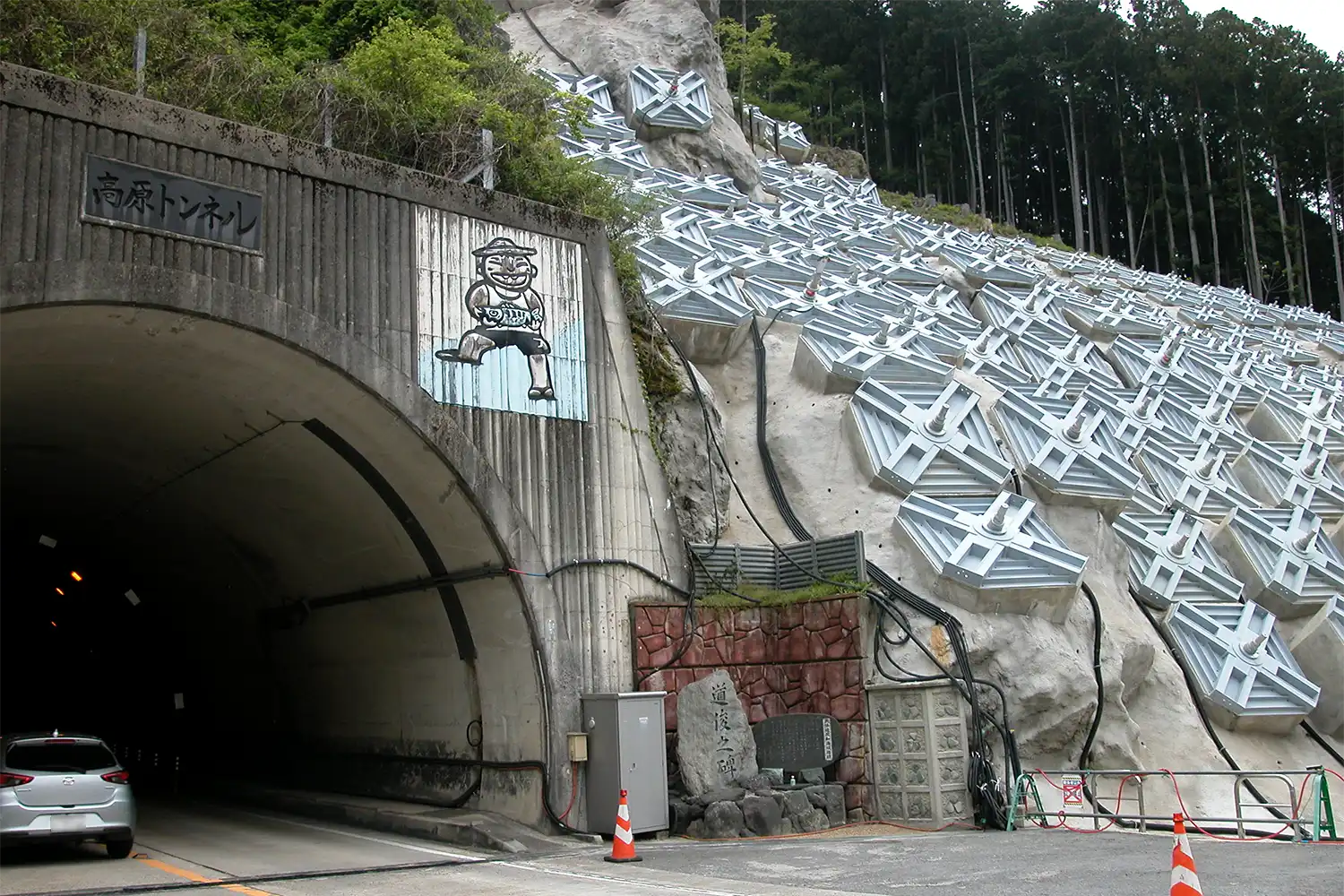 高原トンネル入り口の地滑り対策工事現場。山肌を覆う四角形がアンカー工の1本1本＝2024年4月26日、奈良県川上村（車のナンバーをぼかしています）