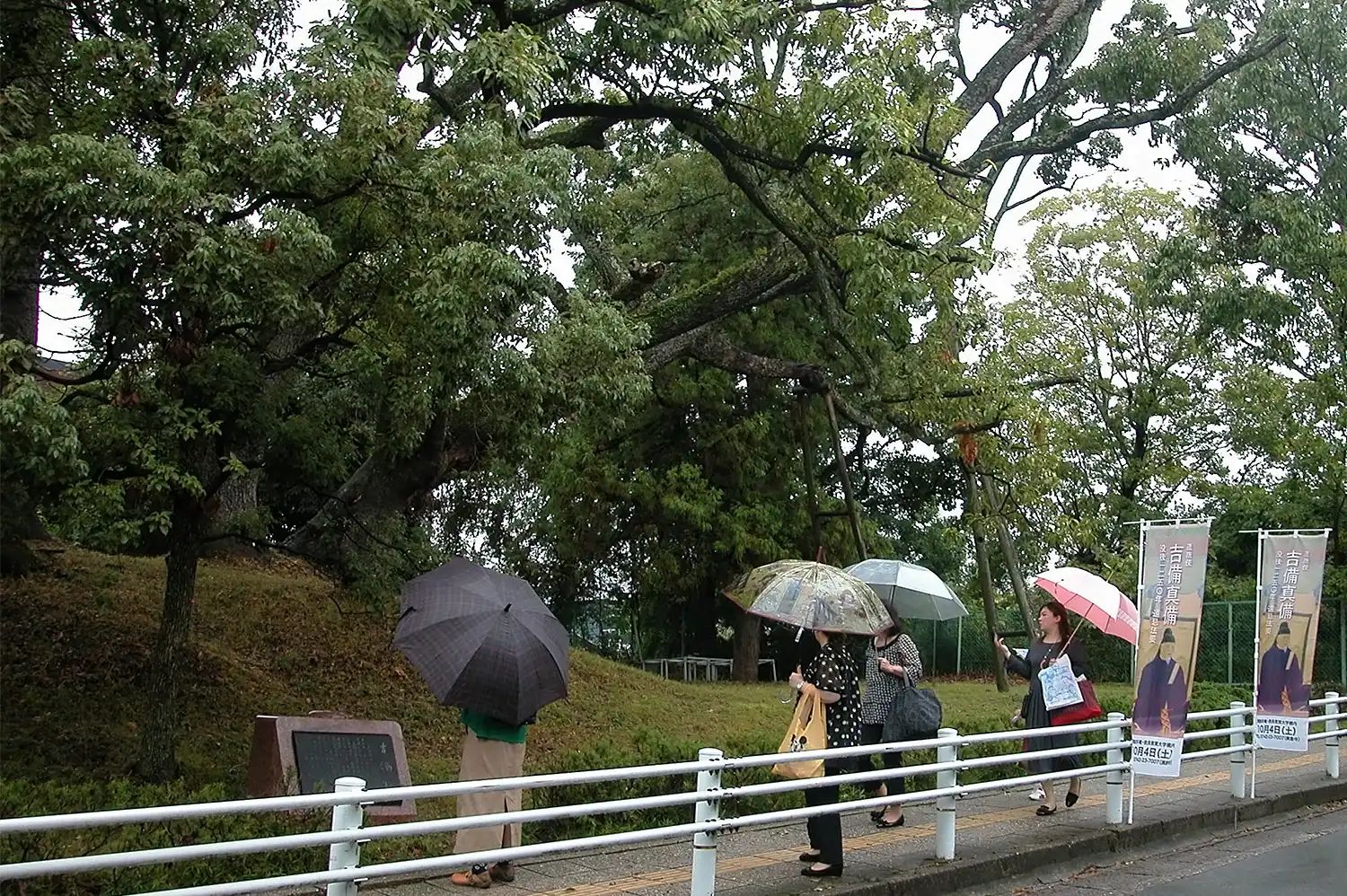 吉備塚古墳を見学する法要の参加者。きりりとした表情の真備のイラストが描かれたのぼり旗が立っていた＝2025年10月4日、奈良市高畑町の奈良教育大学、浅野詠子撮影